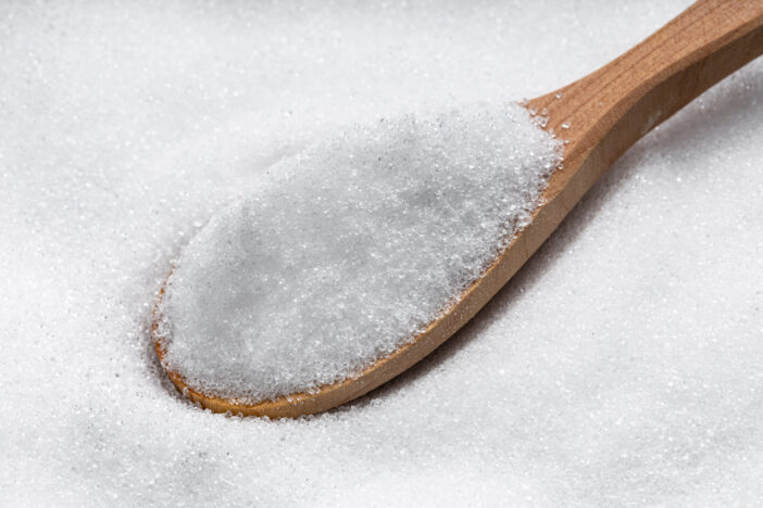 above view of wooden spoon with crystalline erythritol sugar substitute close up on pile of sugar