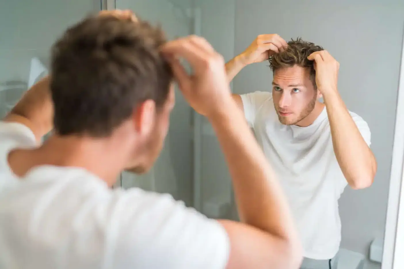 A man looks at himself in the mirror and styles his hair