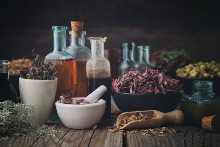 Bottles of healthy tincture or infusion, mortar and bowls of medicinal herbs on wooden table. Herbal natural dyes.