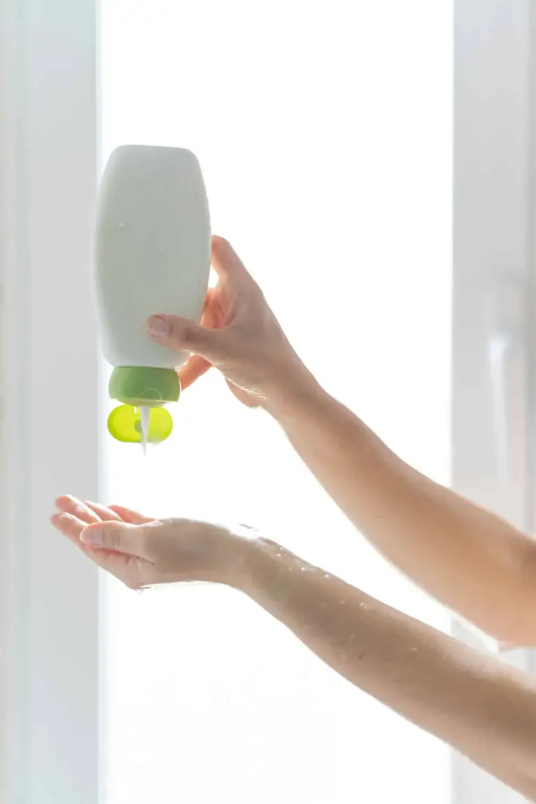 A bottle of shampoo is held in the hand in the shower and the product is dispensed onto the hand.