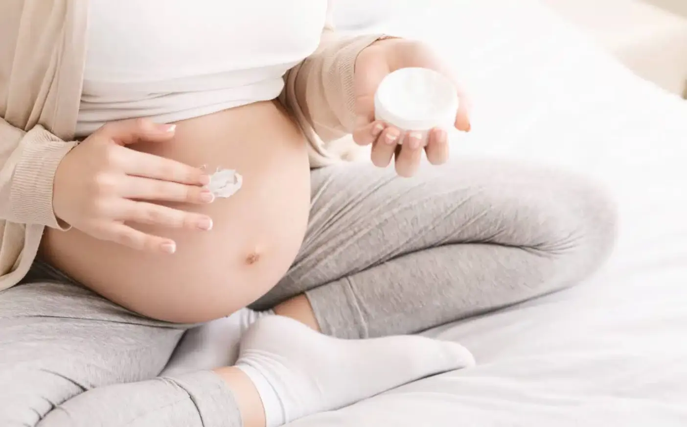 A pregnant woman applies cream to her belly.