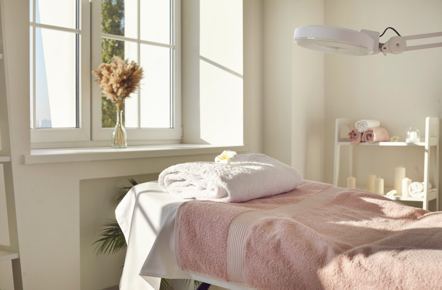 Innenansicht eines neuen, modernen Kosmetiksalons, Schönheitssalons, Massagesalons, Spas oder einer Hautklinik, mit einer leeren Liege, die mit einem frischen weißen Handtuch bedeckt ist und an einem sonnigen Tag von einer Lupenlampe beleuchtet wird